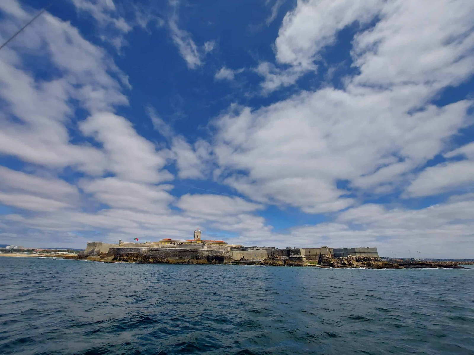 Vue depuis la mer sur le fort de S. Julião da Barra, avec un ciel bleu et des nuages blancs