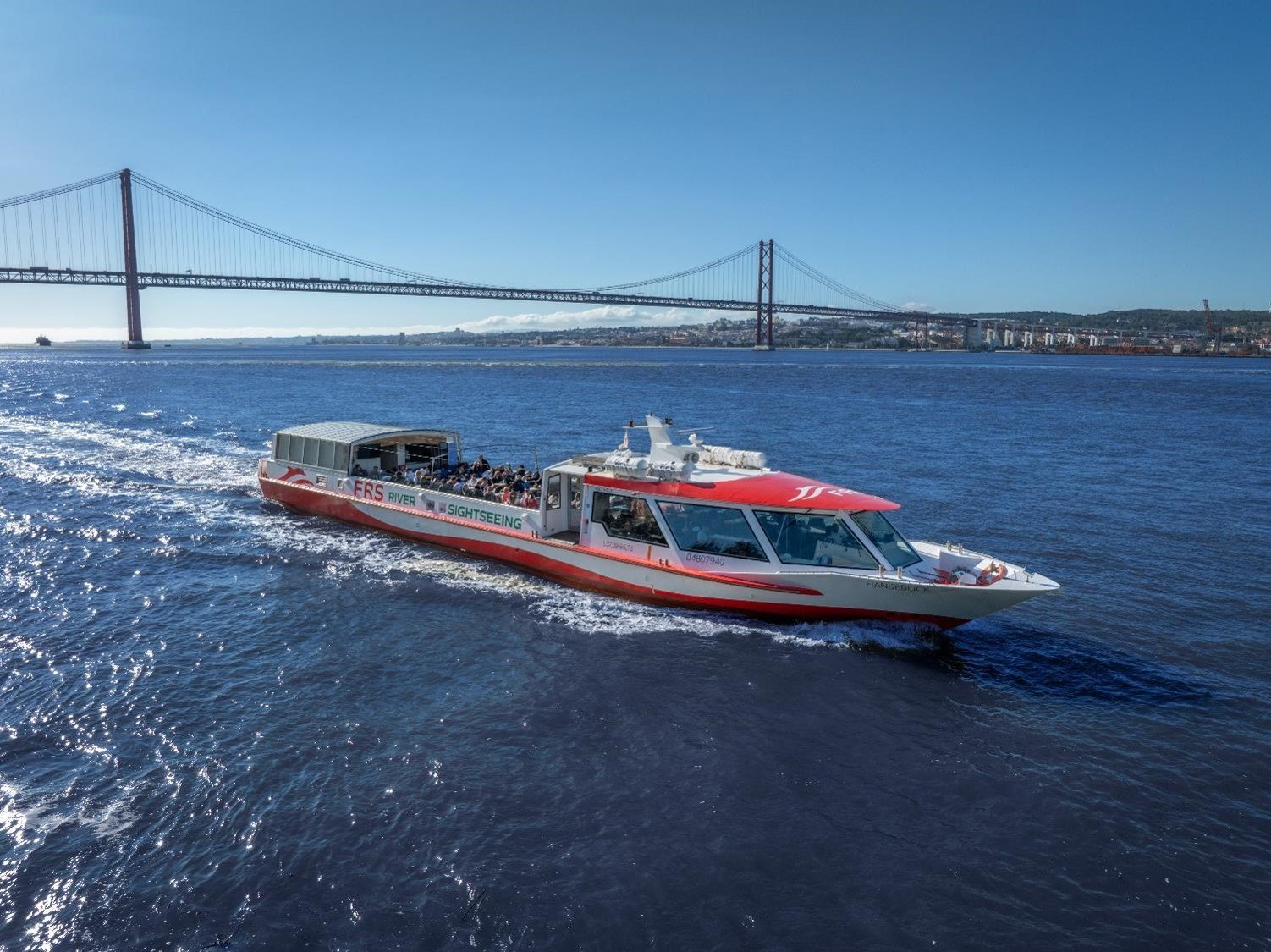 Vue extérieure du bateau à moteur Hanseblick naviguant sur le Tage, avec le pont du 25 avril en arrière-plan. Un bateau de 122 pieds idéal pour les grands événements à Lisbonne.